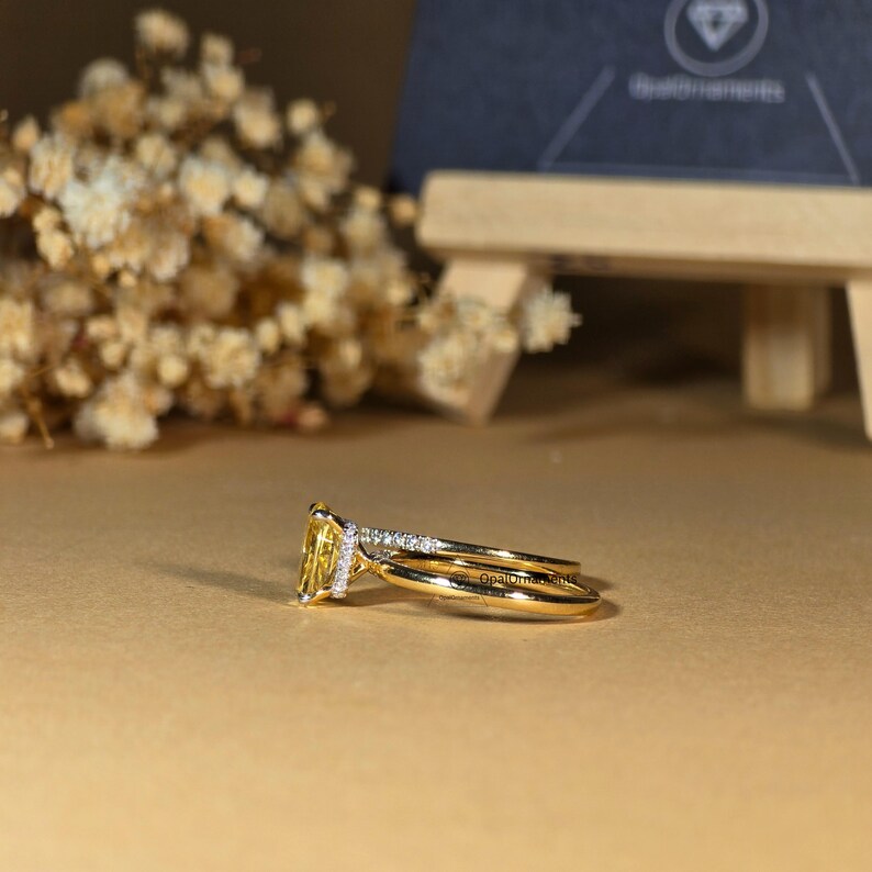 May include: A yellow gold engagement ring set with a large, rectangular, yellow gemstone surrounded by smaller diamonds. The ring is paired with a matching yellow gold band.