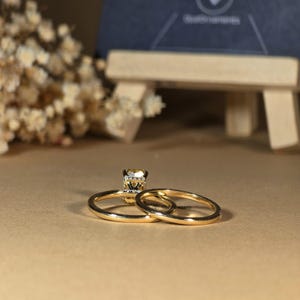 May include: A gold wedding band set with a sparkling diamond engagement ring. The engagement ring has a square-shaped diamond with smaller diamonds surrounding it.