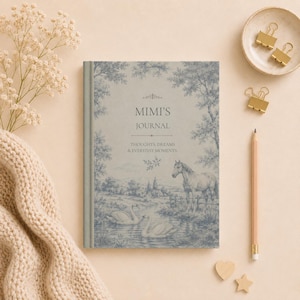 May include: A journal with a blue and white landscape design featuring a horse, swans, and trees. The cover reads "MIMI'S JOURNAL" with the text "THOUGHTS, DREAMS & EVERYDAY MOMENTS." The journal is next to a pencil, gold binder clips, and wooden shapes.