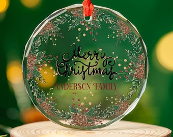 May include: A clear glass Christmas ornament with a gold and green floral design. The ornament has the text "Merry Christmas" and "Anderson Family" written on it.