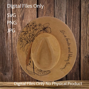 Op de afbeelding: Een bruine cowboyhoed met een zwart bloemenontwerp en de tekst "It's a boots and bling thing..." gedrukt op de zijkant.