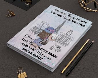 May include: A white journal with a glittery finish features a drawing of a woman in a hat and a scooter in front of the Eiffel Tower. The text on the journal reads "The best things in life are the people we love. Olivia The places we've been and the memories we've made."