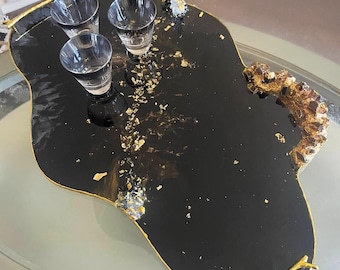May include: Black serving tray with gold accents and three small glass cups. The tray is shaped like a freeform organic shape with a gold twig handle.