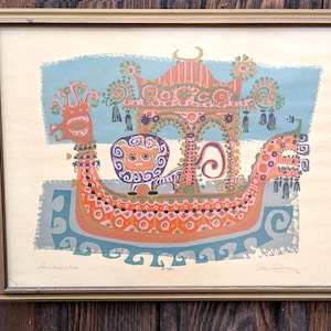 May include: Framed vintage print featuring a colorful, stylized boat with a lion figure and ornate details. The artwork has a light blue and orange color scheme, with a gold frame. The print includes text in the lower left corner.