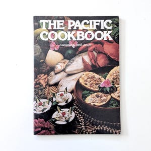 May include: The Pacific Cookbook by René Jansen. The cover displays a colourful collage of Pacific cuisine, including fish, crab, and various dishes. The title is in large white letters, with a vibrant background of food and flowers.
