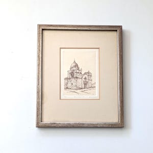May include: Framed sepia-toned architectural print of a domed building, likely a church or mission. The print is set within a cream-colored mat and a silver-toned wooden frame. The artwork is a detailed pen and ink drawing.