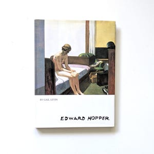 Puede incluir: Portada de libro con una pintura de Edward Hopper. La obra muestra a una persona leyendo en una cama. La portada tiene el nombre del artista en fuente manuscrita y el nombre del autor en la parte superior.
