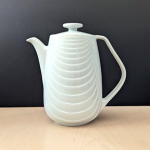 Op de afbeelding: Witte keramische theepot met een geribbeld ontwerp en een gebogen handvat.