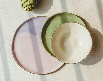 Puede incluir: Tres platos de cerámica con bordes dorados. El plato más grande es rosa claro, el plato del medio es verde y el plato más pequeño es blanco. Los platos están apilados uno encima del otro.