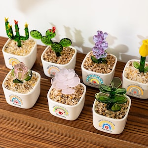 May include: A white ceramic mug with a black handle and the text "But First, Coffee" in a black, handwritten-style font. The mug is on a white surface.