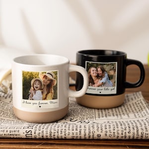 Op de afbeelding: Twee keramische mokken met foto's en tekst. Eén is wit met "I love you forever, Mom" en een foto van een vrouw en een kind. De andere is zwart met "Forever your little girl" en een foto van twee vrouwen. Beide hebben bruine bases.