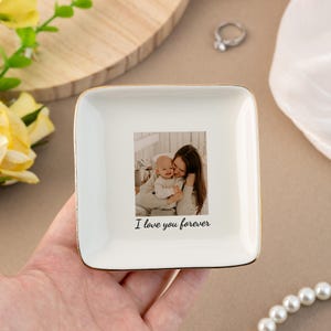 Puede incluir: Plato de cer&aacute;mica blanca para joyas con un borde dorado. El plato presenta una foto de una madre y un hijo con el texto "I love you forever" impreso debajo de la foto.