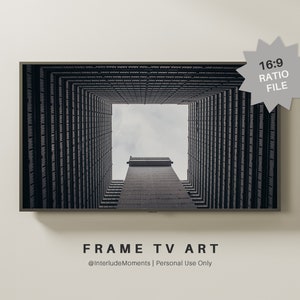 May include: A black and white photograph of a building with a square opening in the center, looking up towards the sky. The building is made of concrete and has a grid pattern. The sky is cloudy and gray. The image is framed in a black frame.