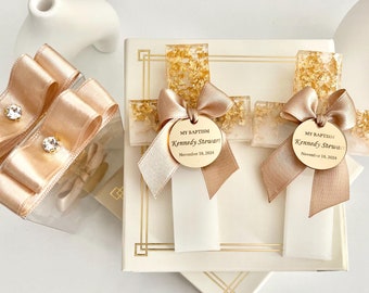 Puede incluir: Dos cruces de bautizo con detalles de pan de oro y una cinta de raso. Cada cruz tiene una etiqueta redonda que dice "MY BAPTISM Kennedy Stewart November 10, 2024". Las cruces están sobre una caja blanca con ribetes dorados.