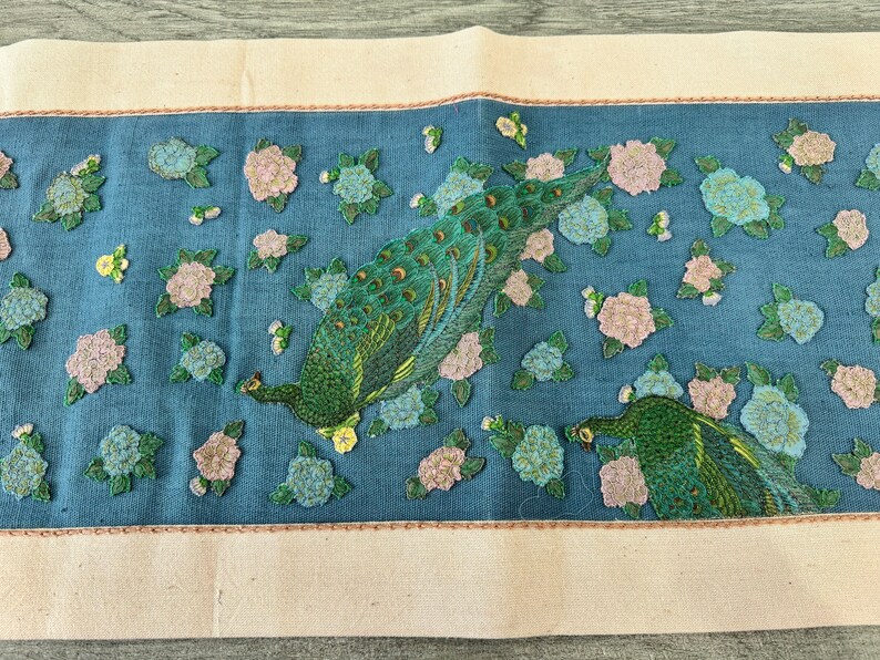 May include: A blue fabric panel with embroidered peacocks and pink flowers. The peacocks are green, blue, and gold. The flowers are pink and white.