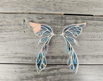 May include: A pair of iridescent blue and white fairy wings with a delicate, intricate design. The wings are made of a thin, translucent material and have a shimmery finish.