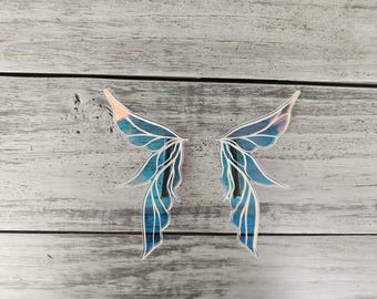 May include: Two iridescent blue and white fairy wings with a delicate, intricate design. The wings are made of a thin, translucent material and have a slightly shimmery finish.