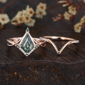 May include: A rose gold engagement ring set with a green moss agate gemstone in a kite shape surrounded by a halo of small diamonds. The band is twisted and features two small green gemstones on each side of the center stone. The matching wedding band is a delicate rose gold band with a v-shaped design.