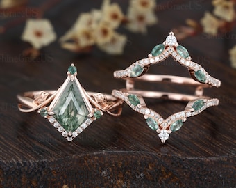May include: A rose gold engagement ring set with a green moss agate center stone and a matching rose gold wedding band with green gemstones and diamonds.