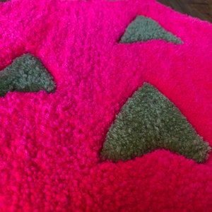 May include: A pink, fluffy rug with green triangle shapes. The rug has a yellow and green flower design at the top.