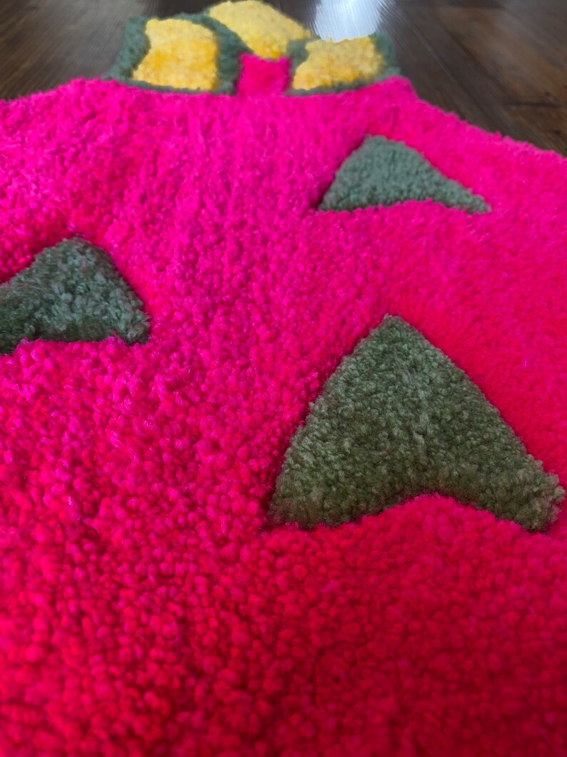 May include: A pink, fluffy rug with green triangle shapes. The rug has a yellow and green flower design at the top.