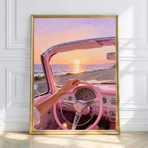 May include: A framed print of a pink convertible car interior with a hand on the steering wheel, driving towards a sunset over the ocean. The car's dashboard and steering wheel are pink, and the sky is a mix of pink, orange, and purple.