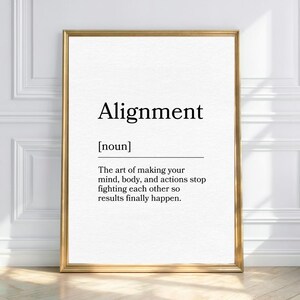 May include: A framed print with the word "Alignment" in a bold, black font. The definition below reads: "The art of making your mind, body, and actions stop fighting each other so results finally happen." The frame is gold.