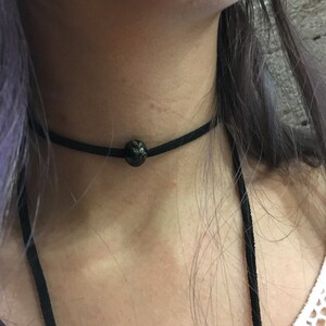 May include: A black choker necklace with a single black bead in the center.