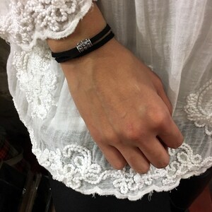 Peut inclure: Un bracelet en cuir noir avec un charme argenté orné d'un motif décoratif.