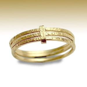 Peut inclure: Une bague en or avec trois bandes, chacune avec une surface texturée. Les bandes sont reliées par un petit morceau de métal rectangulaire.