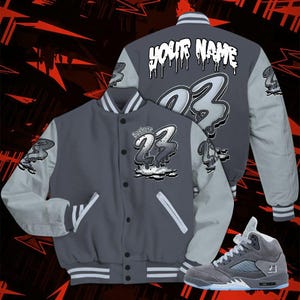 May include: A gray and light gray varsity jacket with the number 23 and the text "Your Name" on the back. The jacket has white stripes on the collar, cuffs, and waist. A matching gray sneaker with the number 23 is also shown.