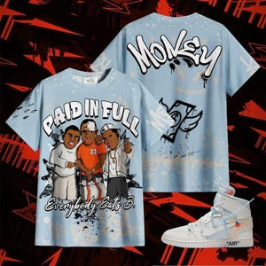 Puede incluir: Camisetas de color azul claro con un gráfico de tres personajes de dibujos animados y las palabras "PAID IN FULL" y "Everybody Eats B." La parte trasera de la camiseta tiene la palabra "MONEY" en estilo graffiti. Un par de zapatillas altas blancas y azul claro también están en la imagen.