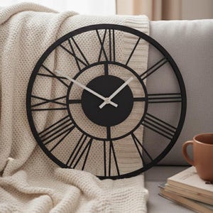 May include: A black, round wall clock with Roman numerals. The clock has a minimalist design with a black face and white hands. The clock is displayed on a neutral-colored background.