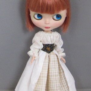 May include: A doll with red hair wearing a white and beige gingham dress with a white lace trim and a black belt.