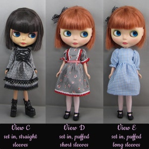 K&ouml;nnte beinhalten: Drei Puppen mit gro&szlig;en Augen und roten oder schwarzen Haaren werden gezeigt. Die Puppen tragen verschiedene Kleider: ein graues Blumenkleid mit schwarzen Stiefeln, ein schwarz-wei&szlig; kariertes Kleid mit roten Akzenten und ein blau-wei&szlig; kariertes Kleid. Der Text unten lautet "View C", "View D" und "View E".
