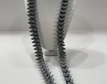 May include: A gray necklace made of small, pointed, triangular shapes. The necklace is displayed on a white mannequin.