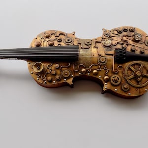 May include: A gold-colored violin with intricate steampunk-inspired details, including gears, pipes, and other mechanical elements.
