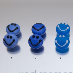 May include: Four pairs of blue glass smiley face beads with black and white details. The beads are arranged in two rows of four, with the numbers 1 through 4 below each pair.