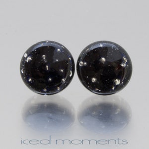 May include: A pair of black glass stud earrings with silver flecks. The earrings are round and have a smooth, glossy finish.