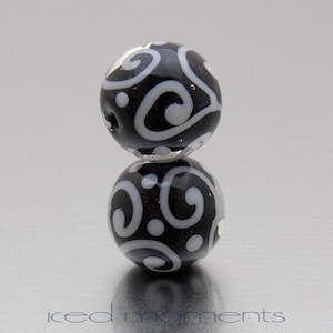 May include: Two black glass beads with a white swirl pattern. The beads are stacked on top of each other.