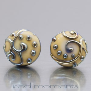 May include: A pair of yellow and gold earrings with a swirl design and small gold dots. The earrings are round and have a shiny finish.