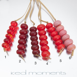 May include: Six strands of glass beads in various shades of red and pink. The beads are strung on a cord and are numbered 1 through 6. The beads are arranged in a gradient from dark red to light pink.