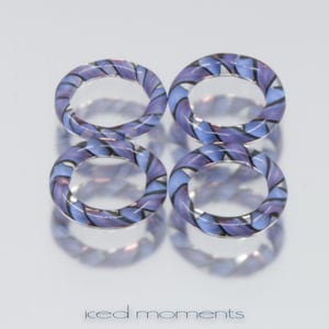 Pode incluir: Quatro anéis de vidro com um padrão listrado roxo e azul. Os anéis estão empilhados uns sobre os outros.