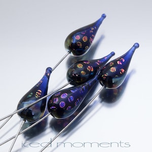 May include: Five iridescent blue glass teardrop beads with black and gold flecks on silver wire.