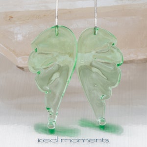 May include: A pair of green glass earrings shaped like wings. The earrings are hanging from silver hooks.