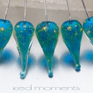 May include: Five teardrop-shaped glass ornaments with a blue and gold speckled finish. The ornaments are suspended from silver wires.