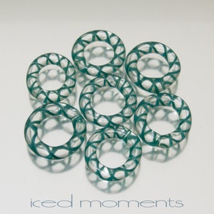 Pode incluir: Sete anéis de vidro verde-azulado com um padrão de cruz. Os anéis estão dispostos em um círculo.