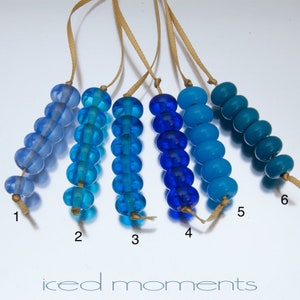 May include: Six strands of blue glass beads, each strand a different shade of blue, from light to dark. The beads are strung on thin brown cords and labeled with numbers 1 through 6.