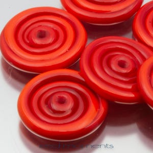 May include: Close-up of several bright red, spiral-shaped glass beads. Each bead has a central hole and a glossy finish. The beads are arranged closely together, showcasing their vibrant color and unique design.