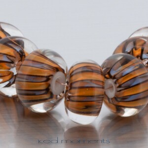 Könnte beinhalten: Nahaufnahme einer Reihe brauner und durchsichtiger Glasperlen mit einem gestreiften Muster. Die Perlen sind rund und haben ein Loch in der Mitte zum Aufziehen.